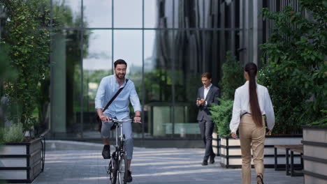 Un-Hombre-De-Negocios-Sonriente-Montando-Bicicleta-En-Un-Moderno-Edificio-De-Oficinas.-Joven-Emprendedor