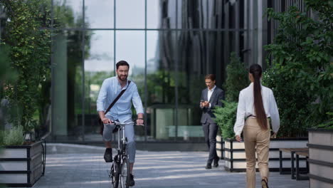 smiling businessman riding bicycle at modern office building. young entrepreneur