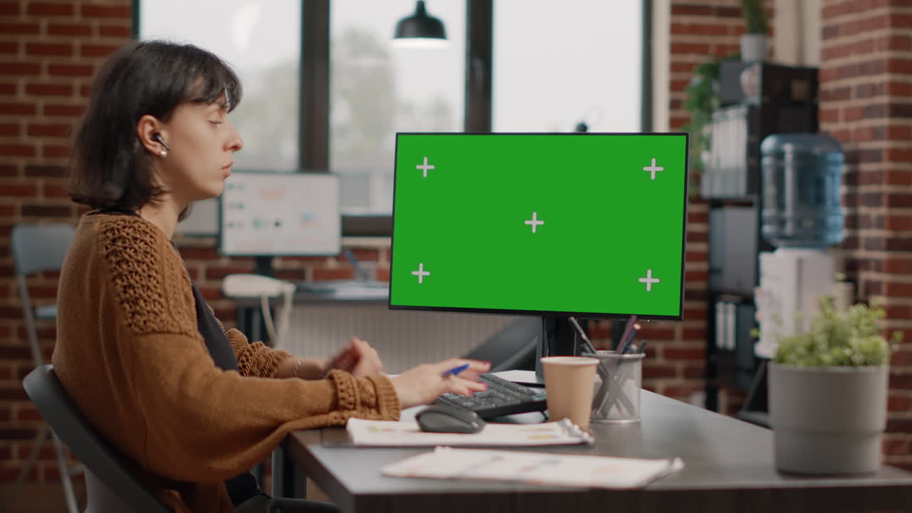 Woman working on a computer with a green screen in the office