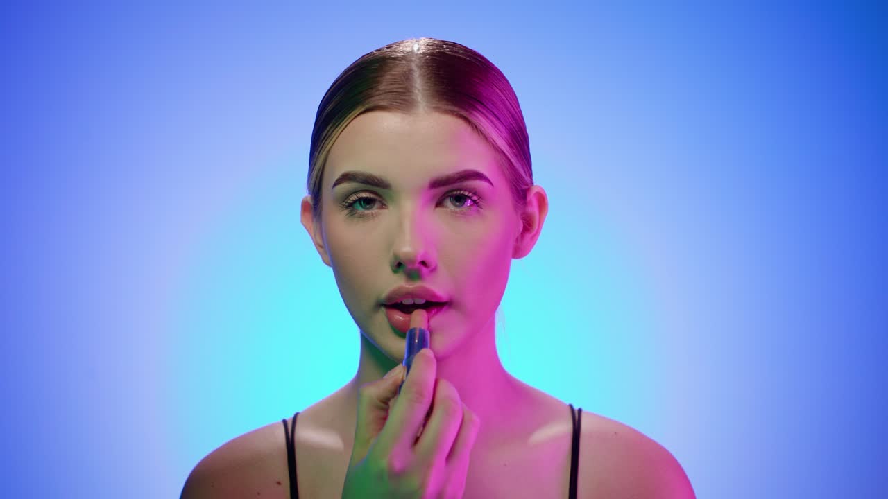 joven mujer rubia caucásica con maquillaje de noche se pone lápiz labial, retrato filmado en el estudio