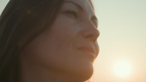 close up of young woman staring into distance during sunset, soft golden sunlight casting gentle glow on her face, contemplative expression, breeze moving hair, flying insects visible