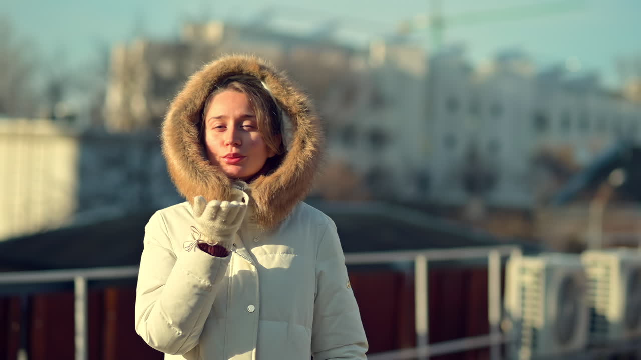 Una donna con indosso un caldo cappotto bianco con cappuccio bordato di pelliccia si gusta una bevanda calda mentre si trova su un tetto. Il sole del mattino splende, proiettando un bagliore caldo sul suo viso.