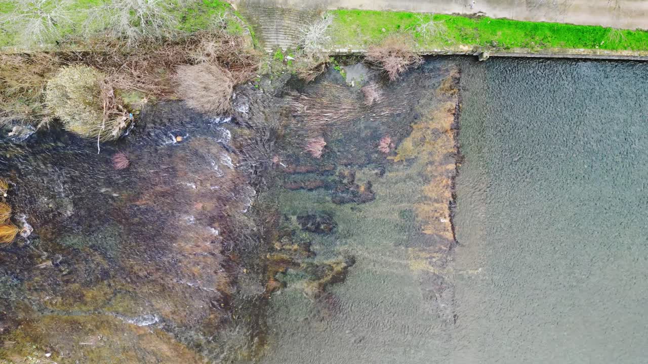 Drone terbang naik di atas sungai jernih di pedesaan Spanyol memperlihatkan pemandangan pedesaan di sekitarnya dengan vegetasi dan tekstur alami di bawah sinar matahari. Konsep perjalanan indah dan alam
