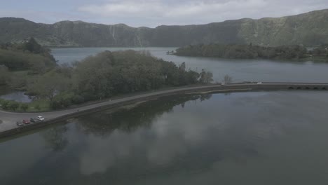 Sete-Cidades-lake-with-a-road-curving-around-the-calm-water-and-lush-green-hills-in-the-background