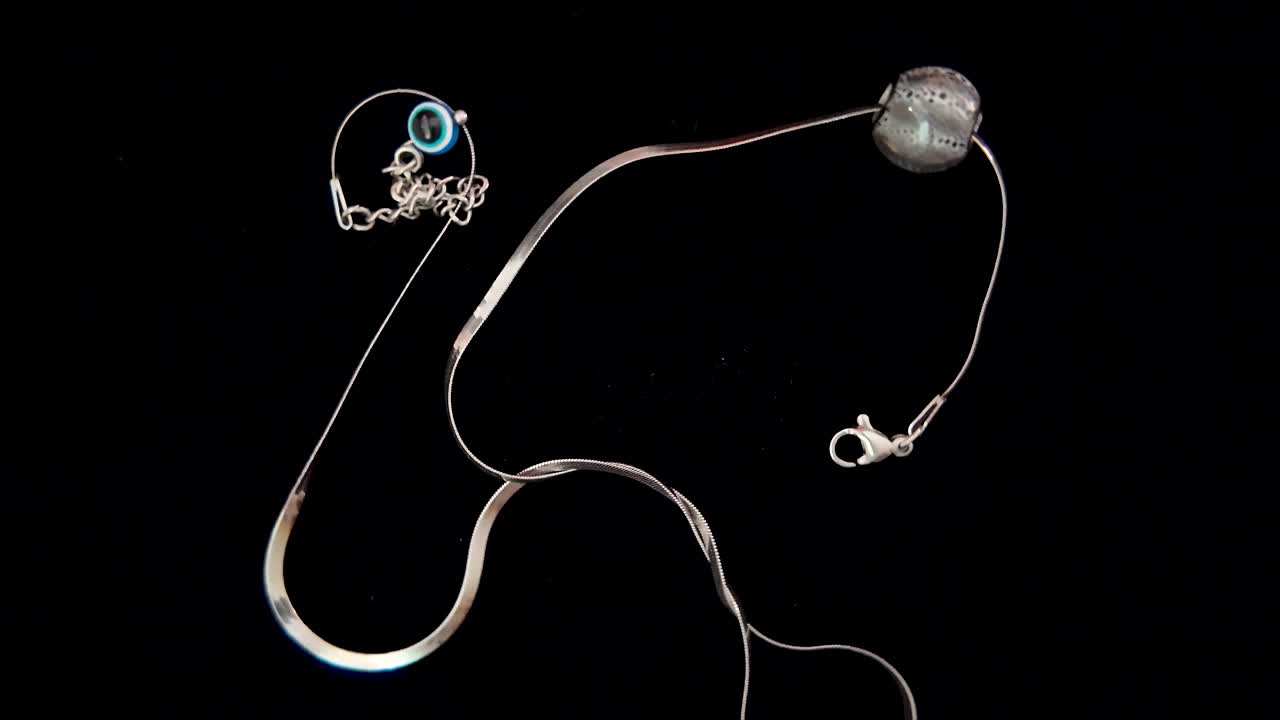 Elegant silver necklace with a blue eye charm slowly rotating against a black background