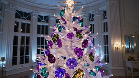 luxury room featuring white christmas tree adorned with colorful iridescent flower ornaments and soft illumination from lamps and spotlights