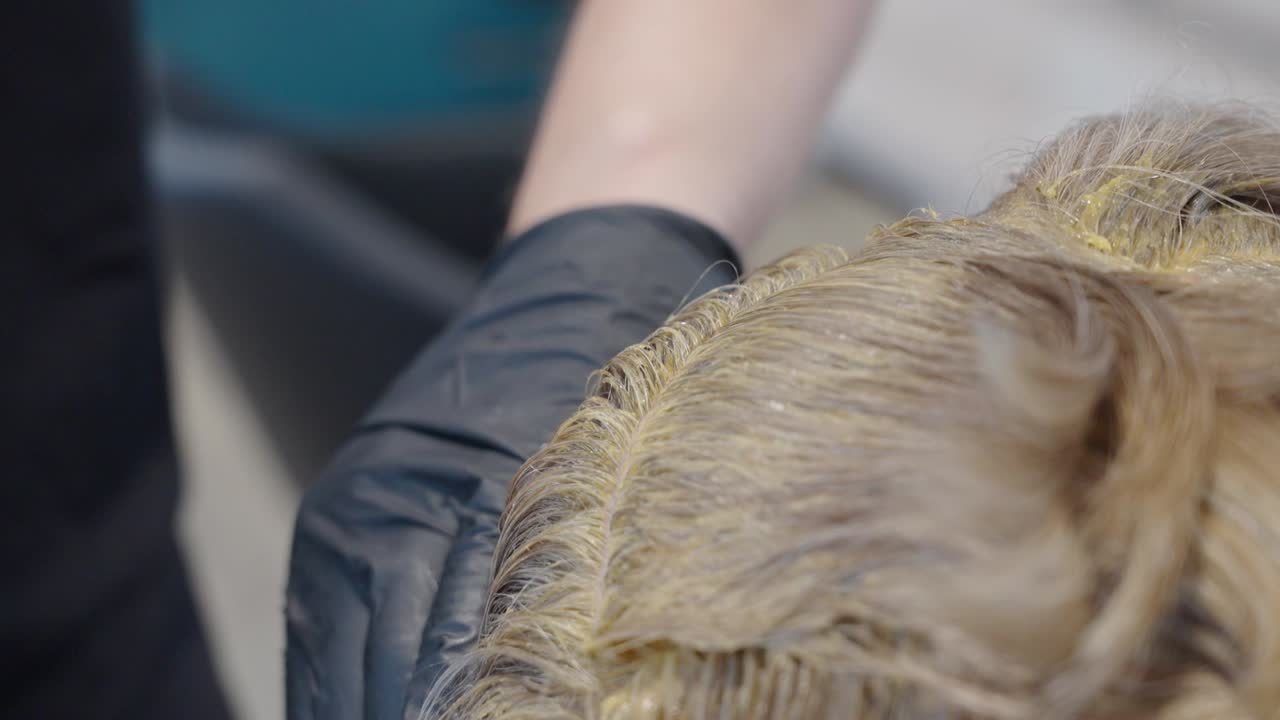 A hairstylist applies bleach paste on several layers of a woman's hair at a salon