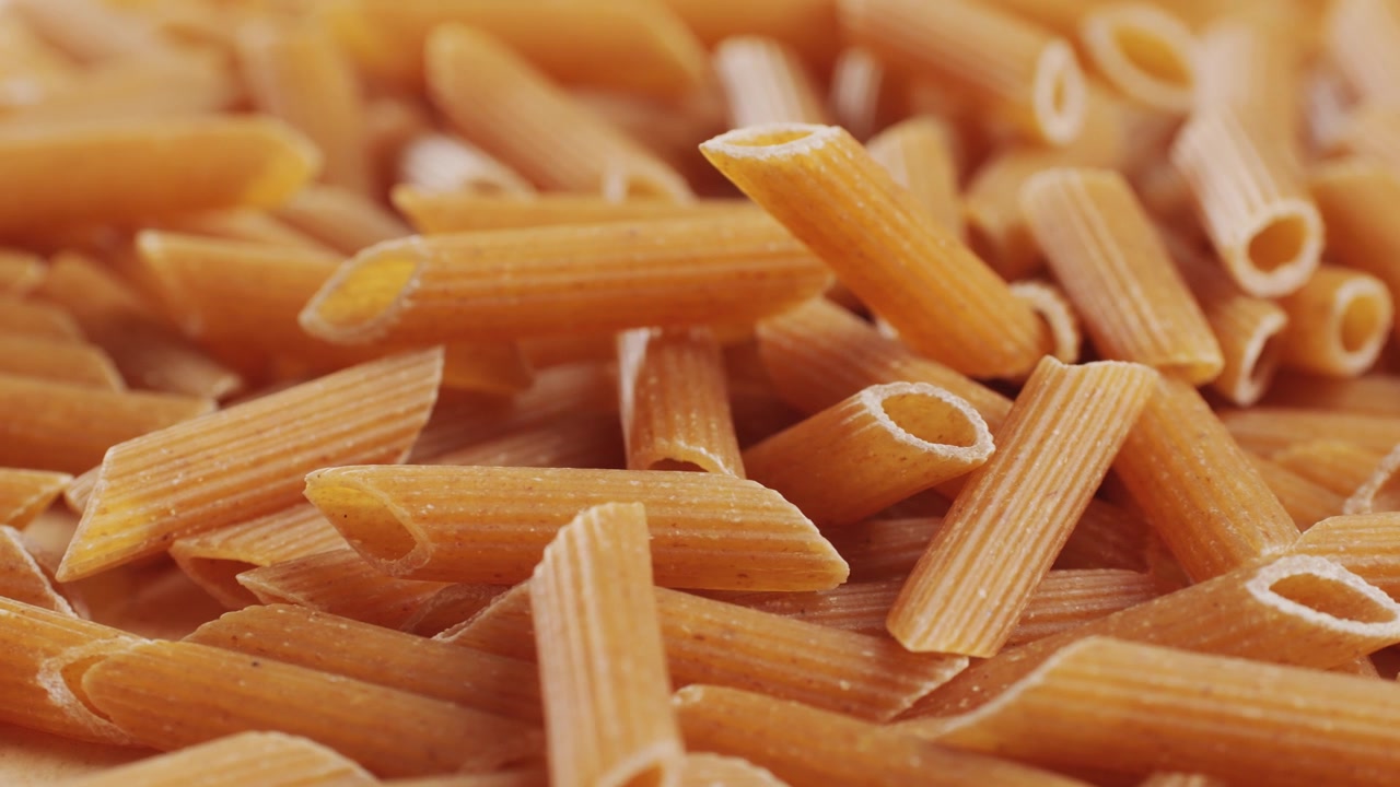Pasta integrale biologica, maccheroni di semola di grano duro, penne rigate crude in una ciotola di legno. Filmato 4k di alta qualità