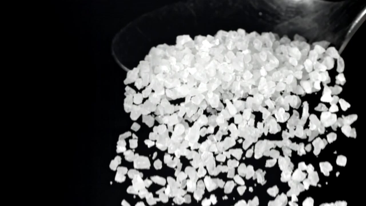 Groft havsalt falder fra en ske i slowmotion