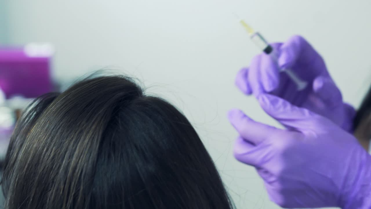 Woman cosmetologist in purple gloves makes the procedure of mesotherapy on woman's head to strength hair and better growth. Brunette girl is doing the injection in hair. Closeup