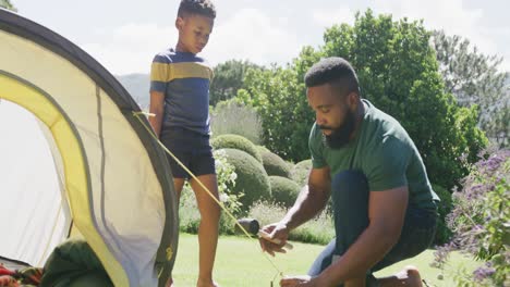 happy african american father and son pitching tent, in slow motion