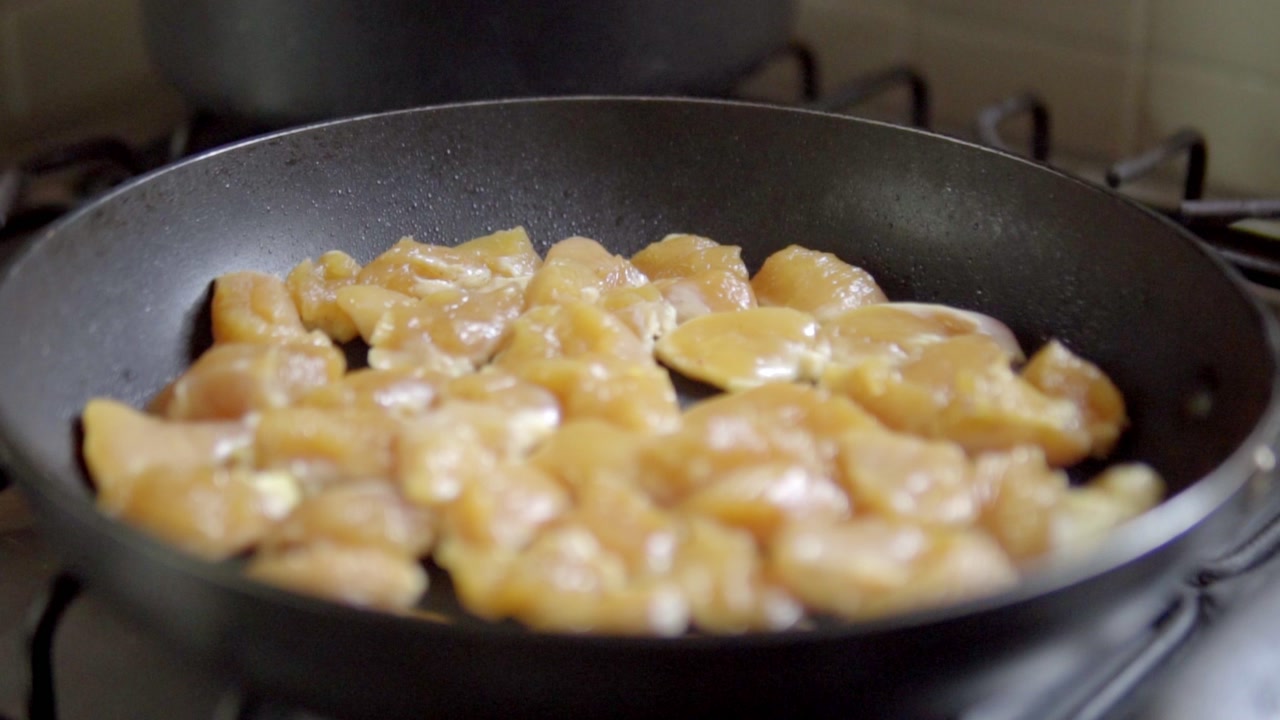 Closeup of chicken pieces cooking in pan showing texture color and heat during meal preparation process in kitchen