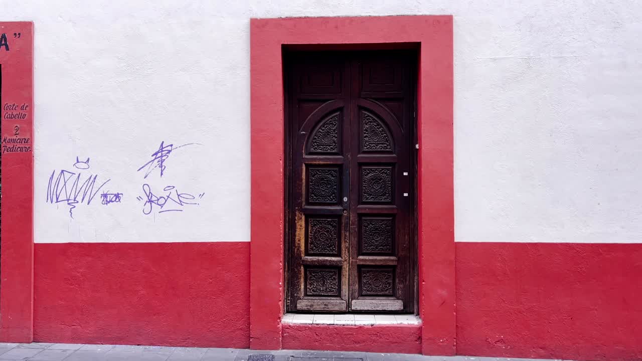 White and red wall with a brown door and graffiti in Cuernavaca center during the day in Morelos, Mexico, wide shot