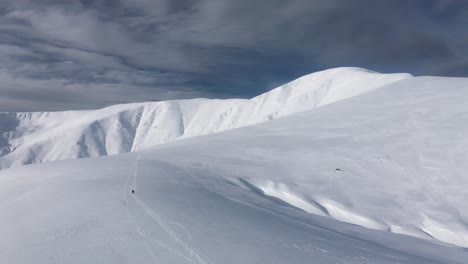 Snow-covered-Papusa-Peak-under-a-cloudy-sky-with-distant-hikers,-Iezer-Papusa-Mountains,-Romania,-wide-shot