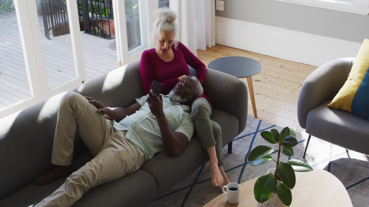 Mixed race senior couple using smartphone in the living room at home