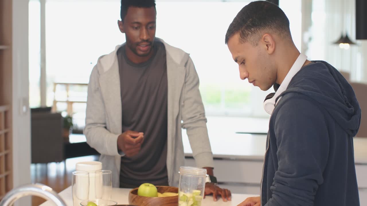 Durante la condivisione di feedback, diversi amici di sesso maschile tagliano verdure in un contenitore del frullatore su un'isola da cucina