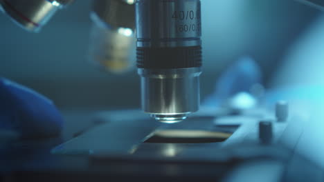 hand of scientist placing glass slide with specimen on microscope stage