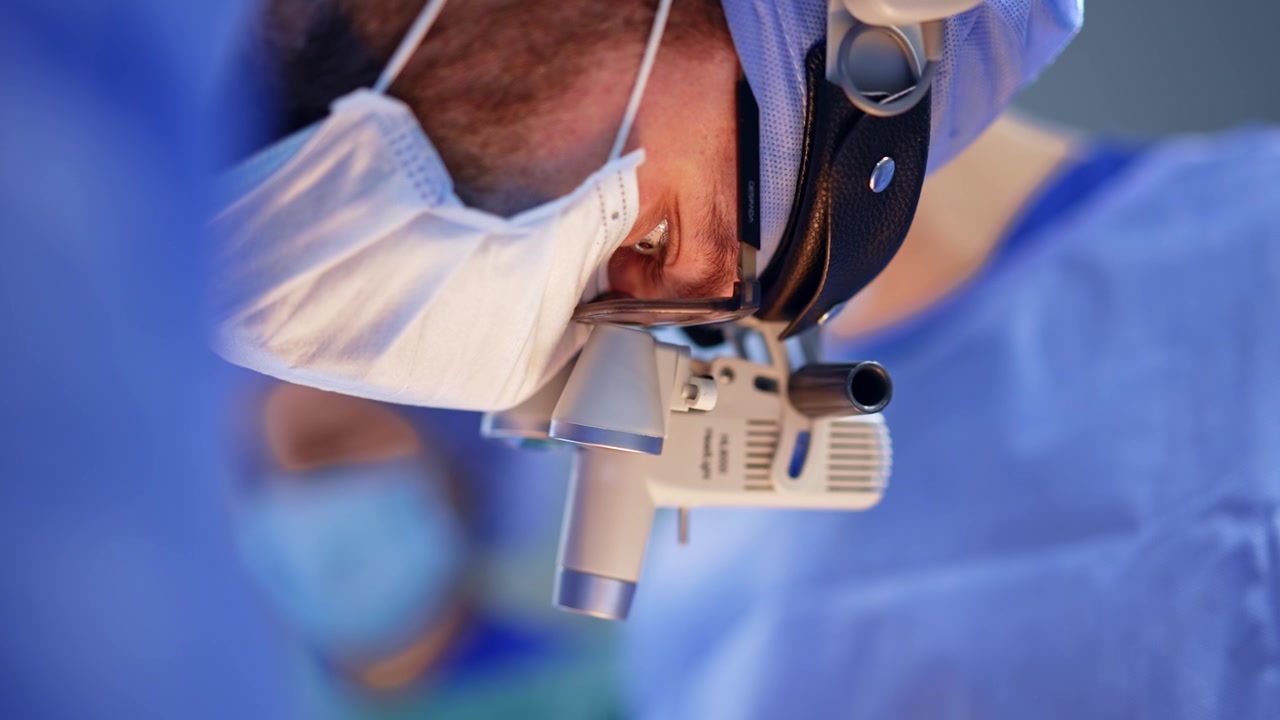 Mirada concentrada del cirujano en la zona de operación a través de las lupas quirúrgicas. Primer plano. Rostro de un médico barbudo en el trabajo