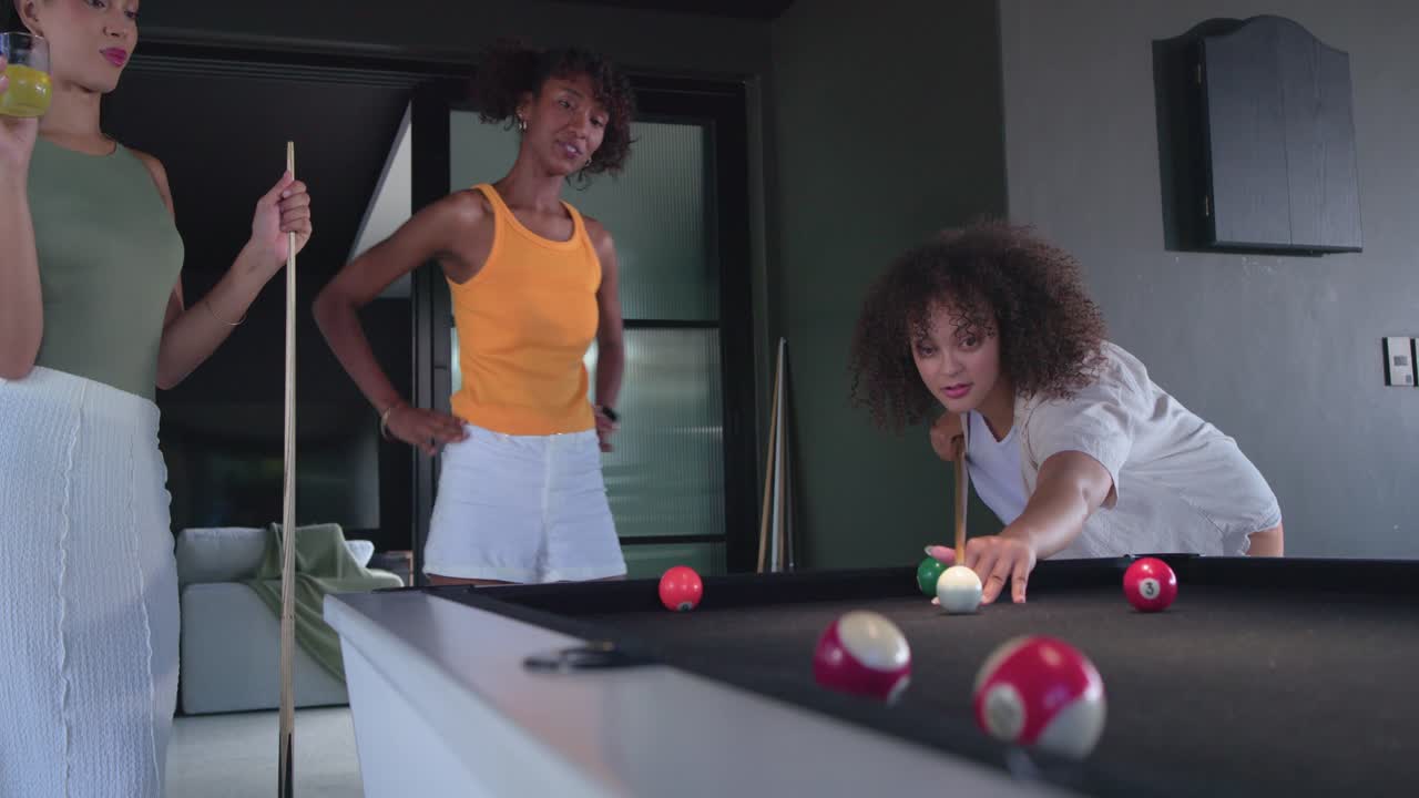 Donne afroamericane dopo aver indicato, mirato e colpito la bilia bianca su un tavolo da biliardo in una lounge per divertimento.