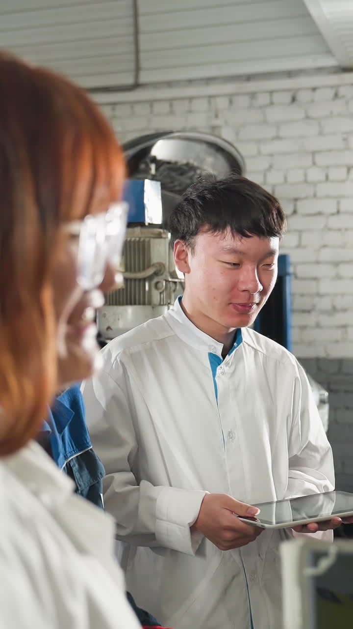 기계공과 실험실 기술자들은 자동차 작업장에서 가운 순간을 나누고, 안경을 쓴 기술자는 태블릿을 들고, 다른 한 명이 배경에서 웃고 있습니다.