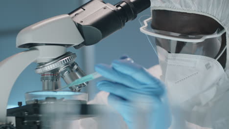 black lab worker in protective suit pouring liquid under microscope