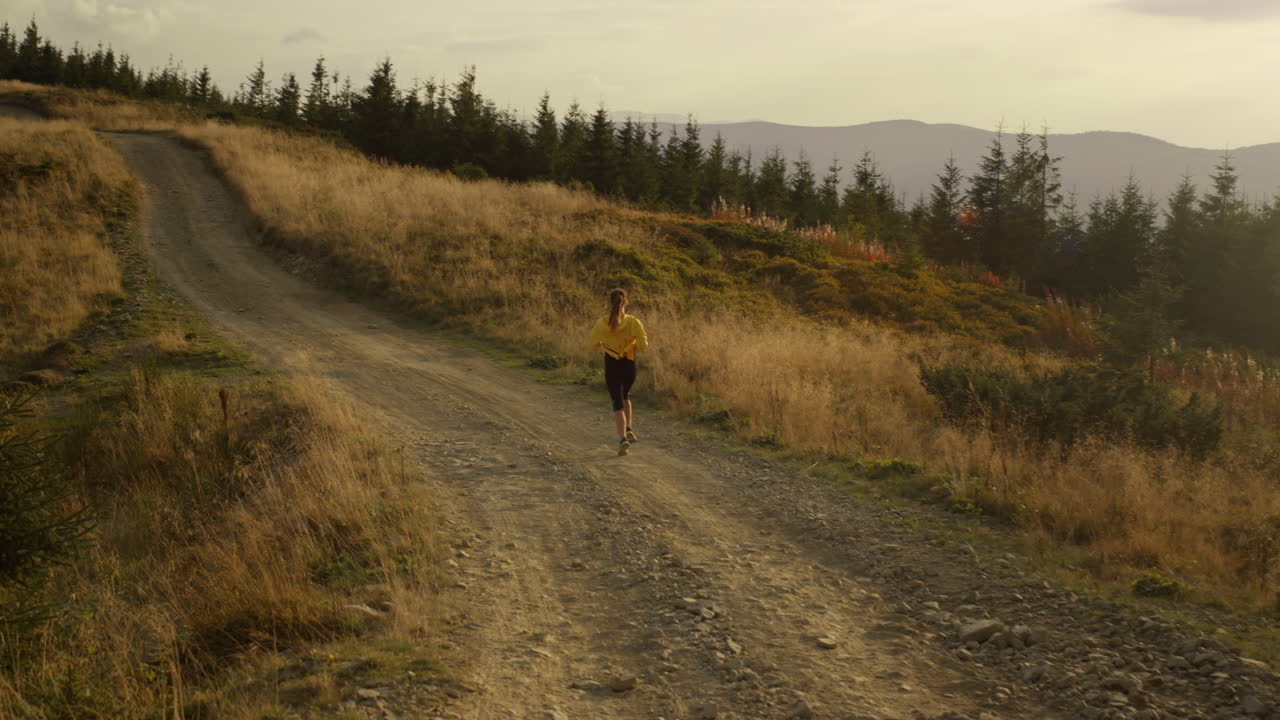 Young woman exercising in natural landscape. Athletic girl jogging on dirty road
