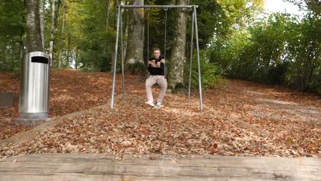 joven balanceándose y saltando del columpio, aterrizando en hojas que caen en el bosque durante el otoño