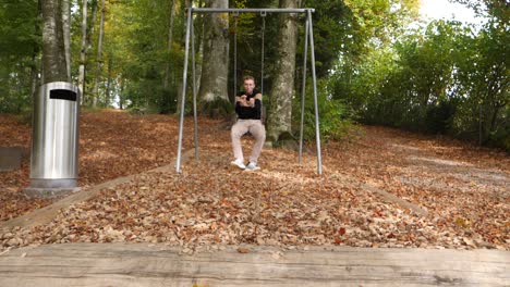 young man swaying and jumping from swing,landing on falling leaves in forest during autumn