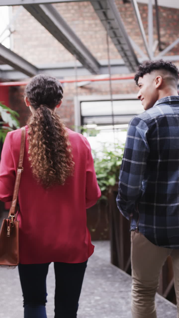 Vertical video of two happy diverse creative designers in discussion in casual office, slow motion