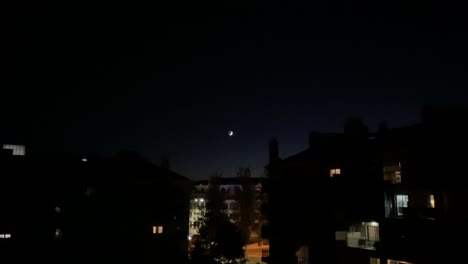 Beautiful-waxing-crescent-moon-setting-behind-city-skyline-buildings-rooftops-at-night