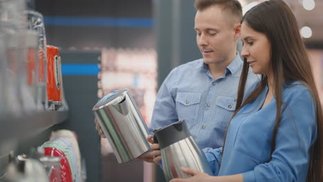 a man and woman hold in their hands an electric kettle in a store choosing before buying in appliances store