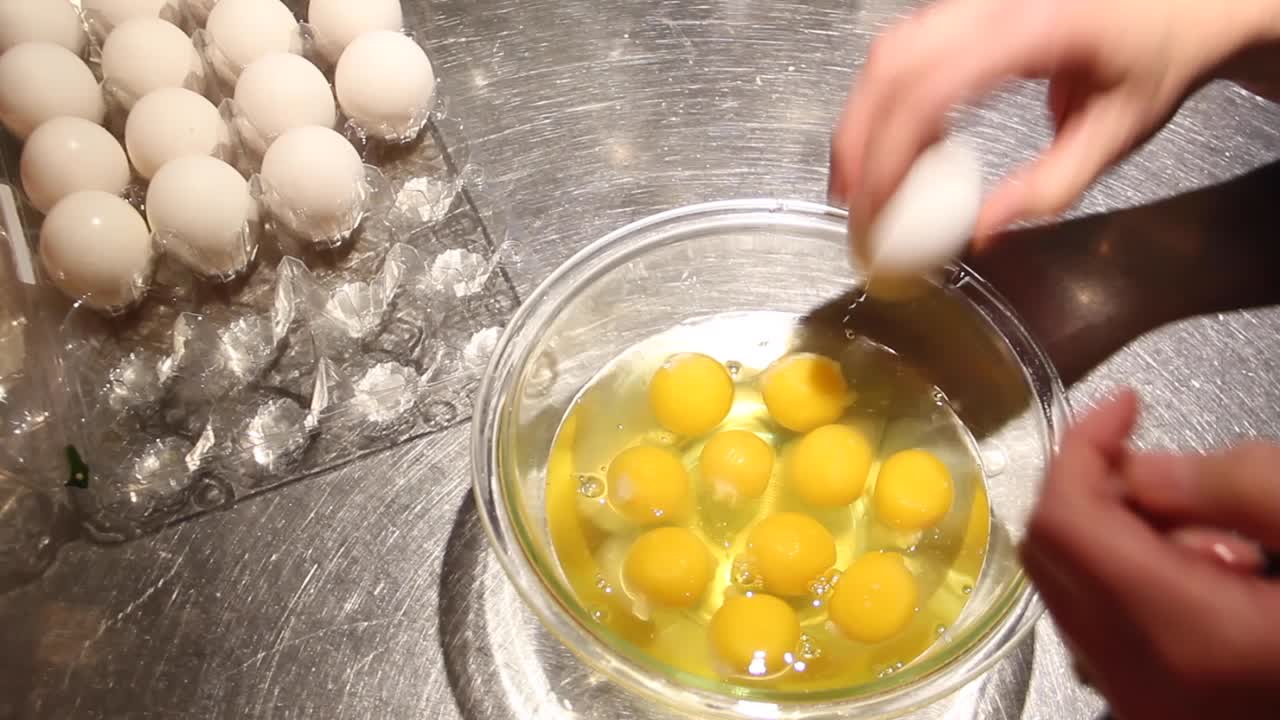 An egg is cracked into a bowl on a clean stainless steel countertop