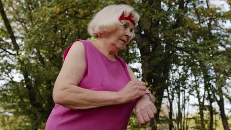 corredora deportiva senior mujer usando reloj inteligente, tocando la pantalla táctil, rastreando el resultado. entrenamiento de fitness