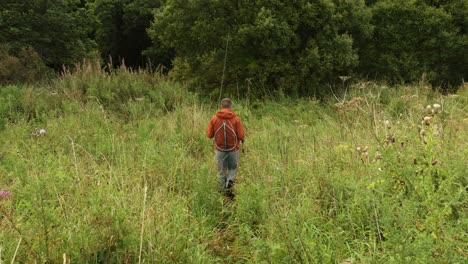 Hand-held-shot-of-a-fisherman-holding-rod-walking-through-waist-high-grass