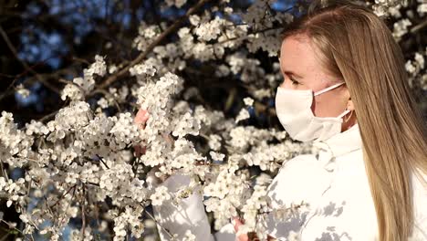 Girl in White Jacket Photographs White Color in Spring Using Smartphone for Photo Blonde Girl in a White Mask Makes a Selfie on a Background of Flowering Fruit Trees Photos for Social Networks