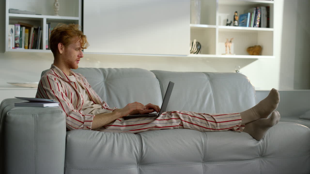 freelancer hablando en línea en casa descansando en pijama. hombre rojo trabajando a distancia