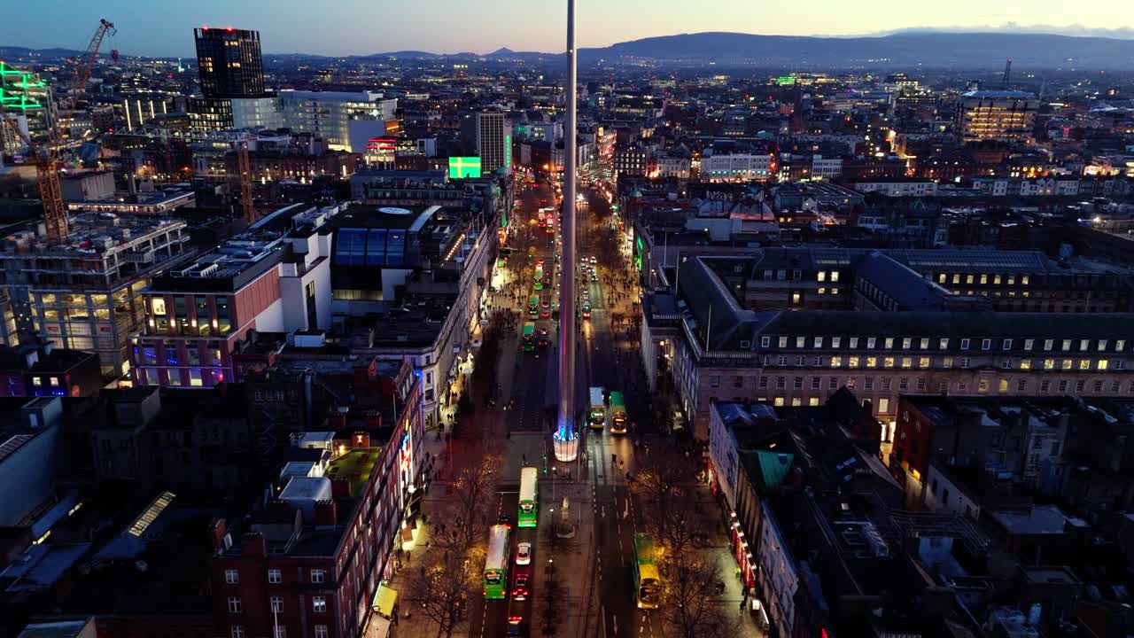 aerial landscape drone shot flying down O'Connell street in Dublin Ireland city with spire landmark in winter nighttime with sun setting and Irish cityscape buildings with illuminated streets