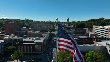 Tattered-American-flag-waving-in-breeze-over-small-town-in-USA