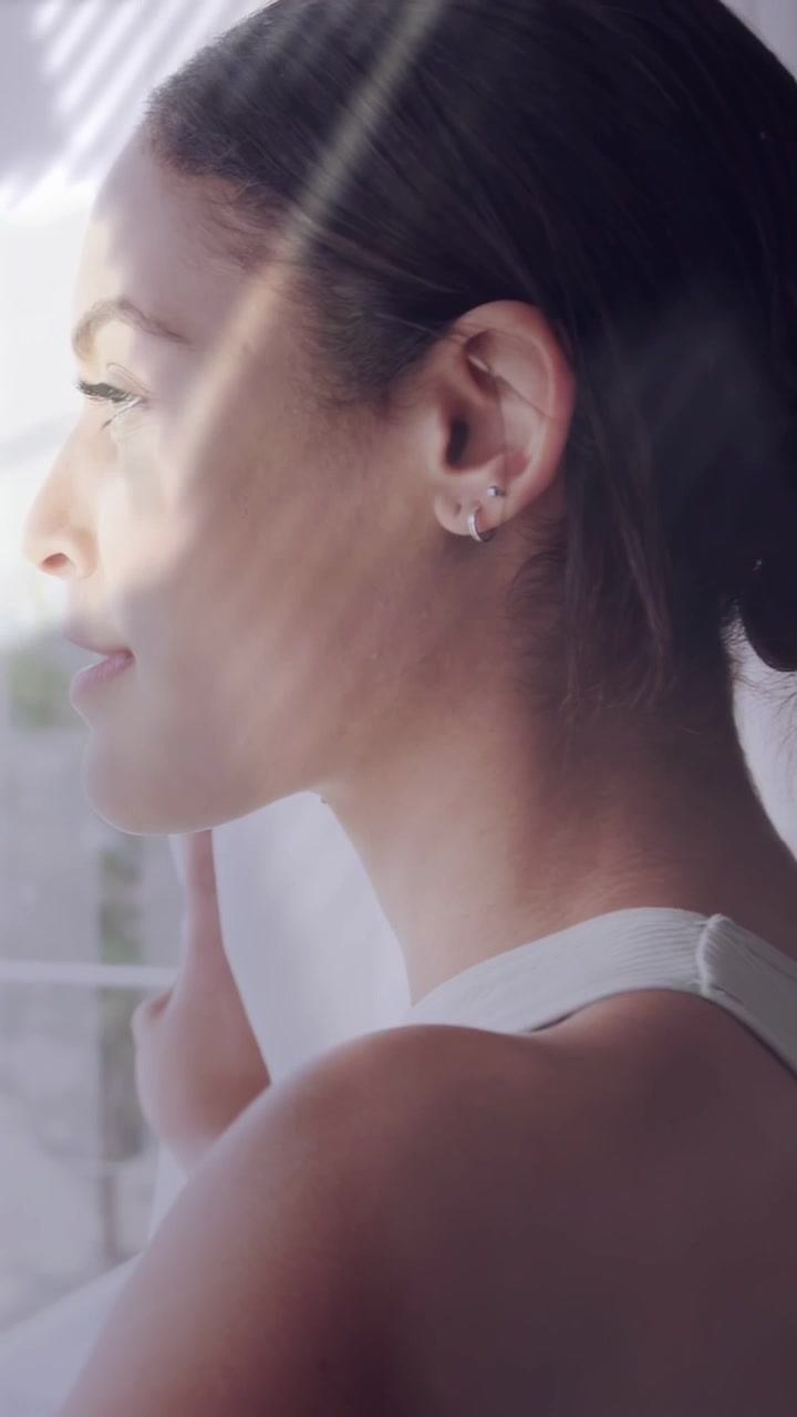 Video verticale: Donna in posa vicino alla finestra che tocca la tenda, il sole crea fasce di luce che le attraversano il viso, marketing