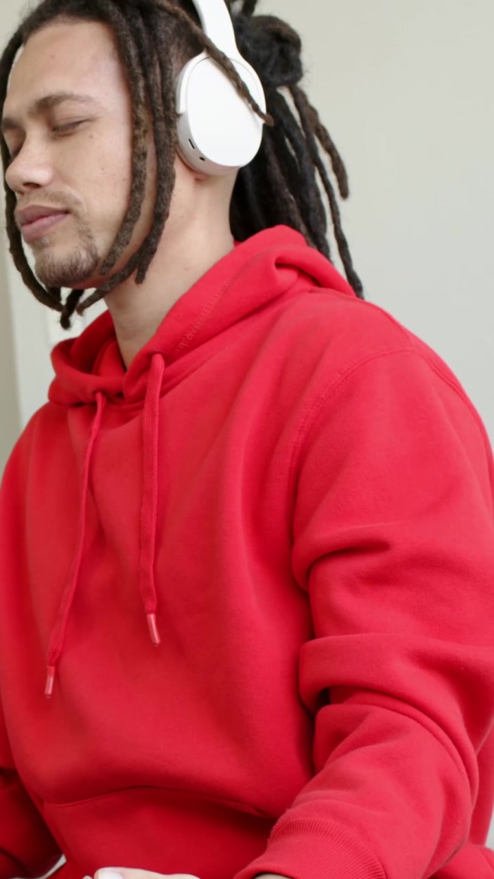 Vertikales Video: Hörender Mann im Studio, Musik beginnt, roter Kapuzenpullover, Kopfhörer, hält Mudra
