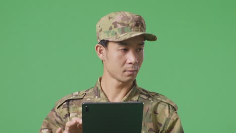 un soldado asiático usando una tableta mientras camina en el estudio de fondo de la pantalla verde