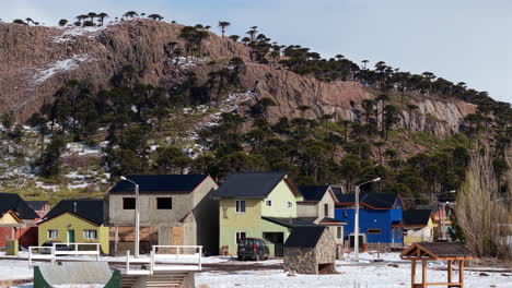 aerial pan of caviahue, argentina, showing colorful houses in snow, set against rocky andean hills and araucaria forests under clear mountain skies