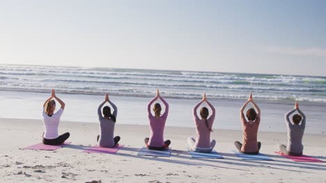 multi-ethnic group of women doing yoga position on the beach and blue sky background