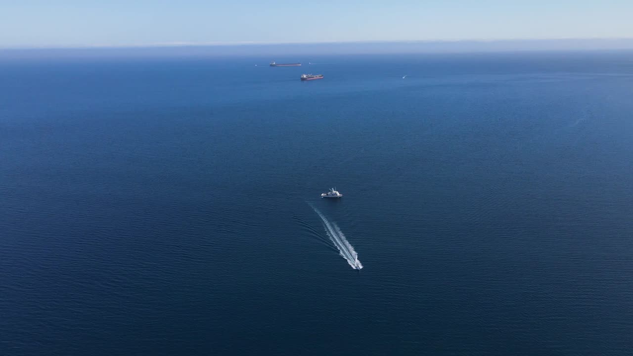 Aerial view of open ocean near Cedros Island, Mexico, featuring a solitary boat driving past transport vessels under a clear sky
