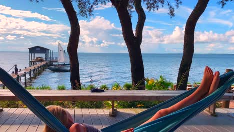 a young girls swings gently in a hammock as she relaxes by the water