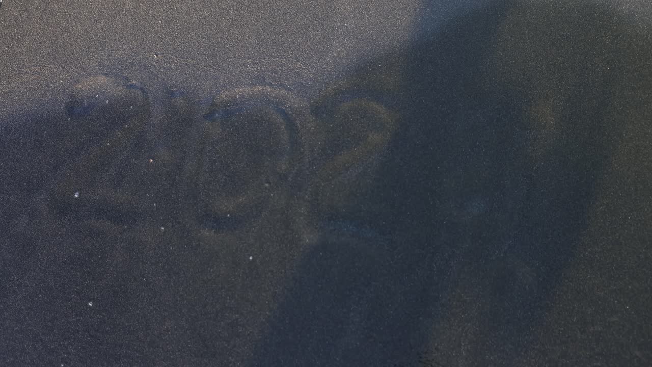 Waves Washing Over '2022' Written on a Dark Sand Beach