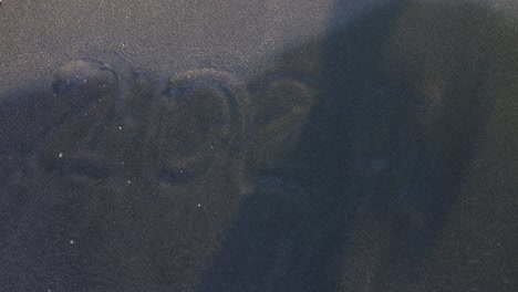 waves washing over '2022' written on a dark sand beach