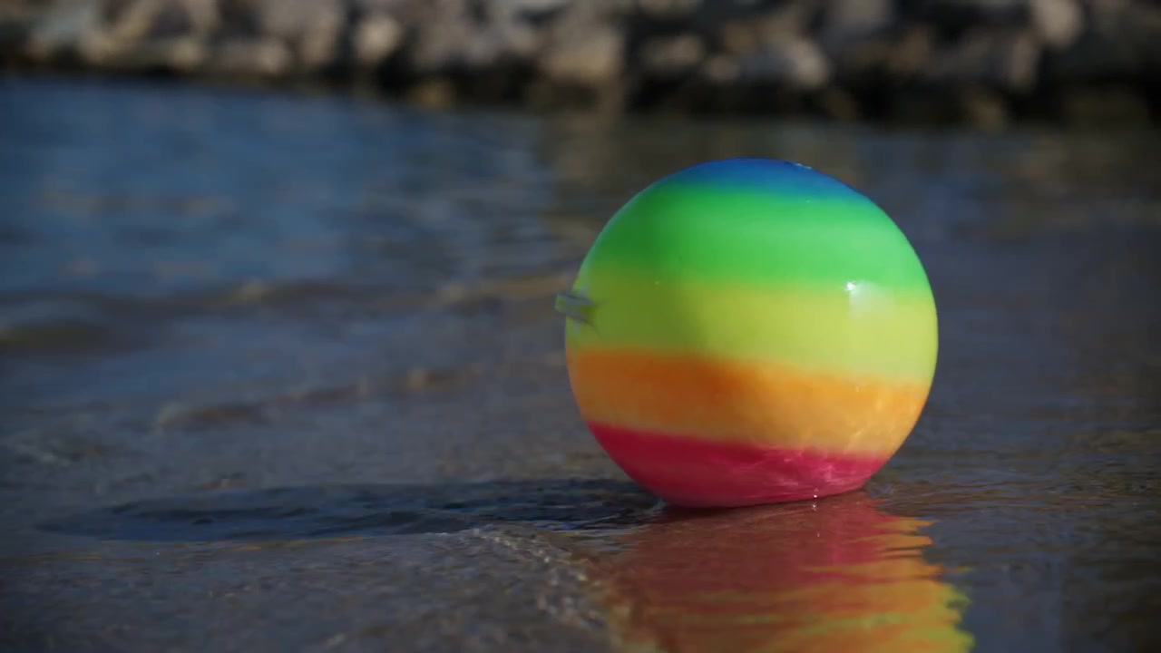 Pelota de playa colorida flotando al borde de olas suaves en la orilla arenosa de Plage de la Gravette en Antibes, Francia, durante un día soleado de verano en la Riviera Francesa