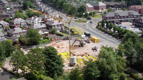 Tall-crane-setting-building-foundation-in-British-town-neighbourhood-aerial-view-above-suburban-townhouse-rooftops,-static-shot