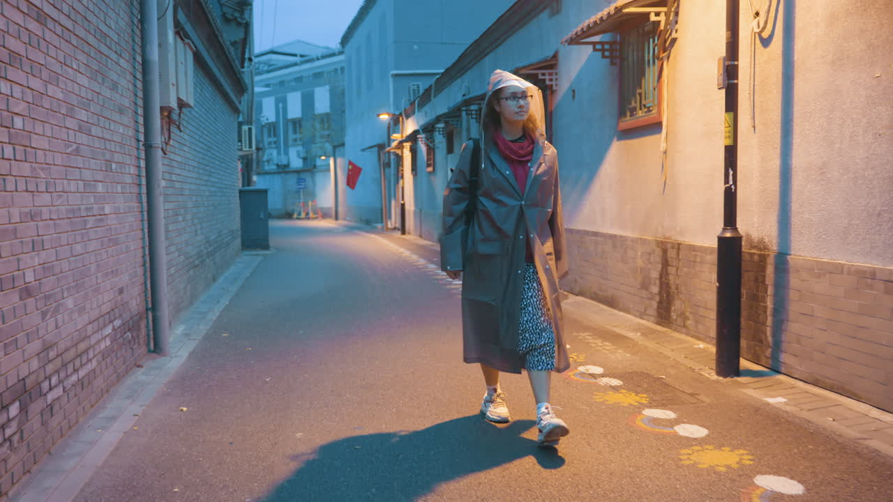 Walking confidently through city streets at dusk. Woman strides with purpose amidst city lights and shadows. An Asian woman moves confidently along busy urban street under street lamp illumination